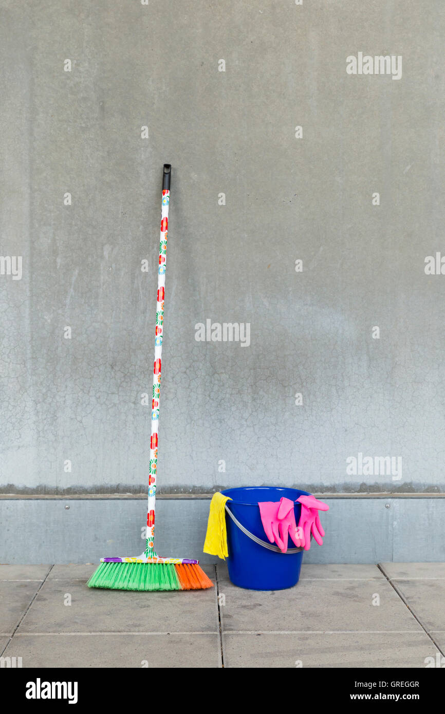 L'équipement de nettoyage colorés (balai, seau, chiffon et gants) en face d'un mur de béton gris, monotone et plancher teint. Banque D'Images