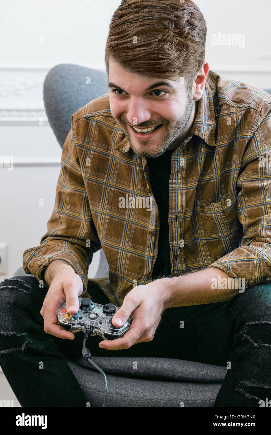 Un jeune homme aux cheveux noirs se penche en avant dans sa chaise tout en maintenant un contrôleur de jeu. Banque D'Images