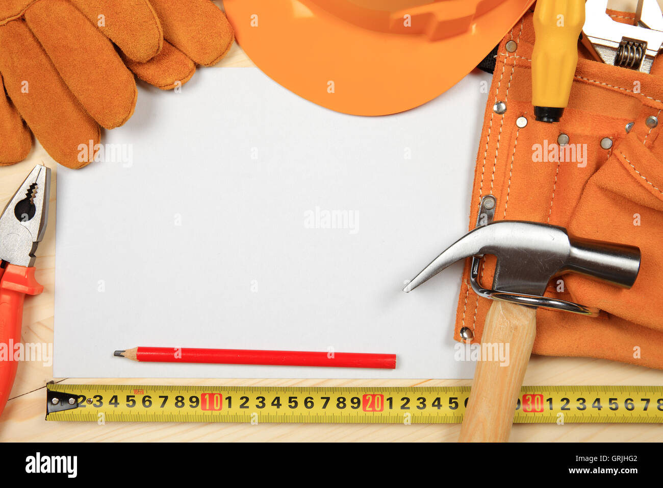 Hard Hat, marteau, pinces, clous, crayon rouge, gants de travail et d'autres outils isolé sur un fond de bois avec une feuille de p Banque D'Images