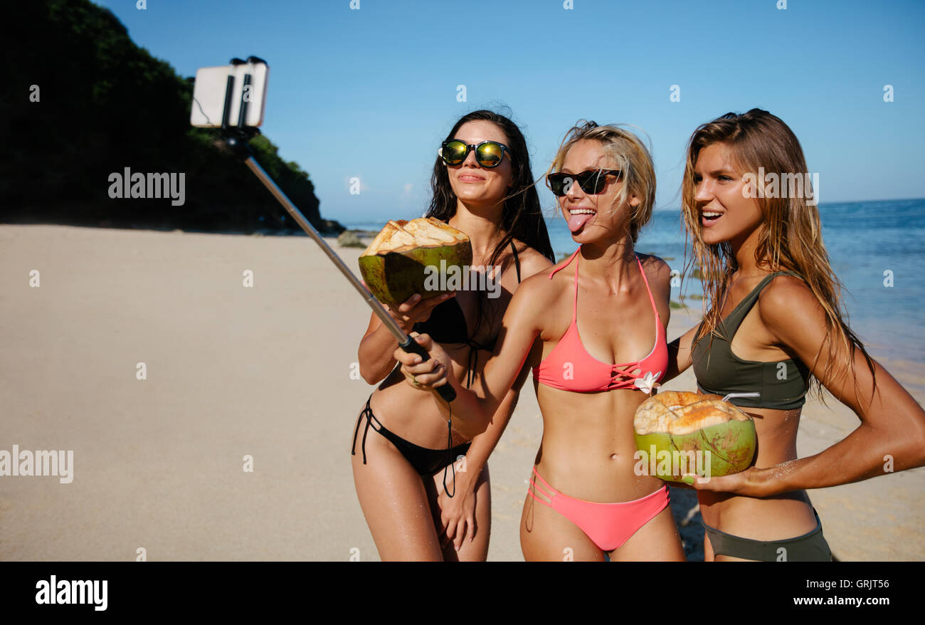 Trois jeunes femmes en bikini sur la plage qui pose pour l'auto portrait. Groupe de femmes friends holding coco et prendre wi selfies Banque D'Images