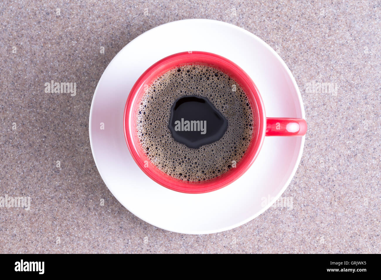 Tasse de café noir énergisant versé dans une tasse rouge sur une soucoupe blanc centré sur un fond en tissu gris Banque D'Images