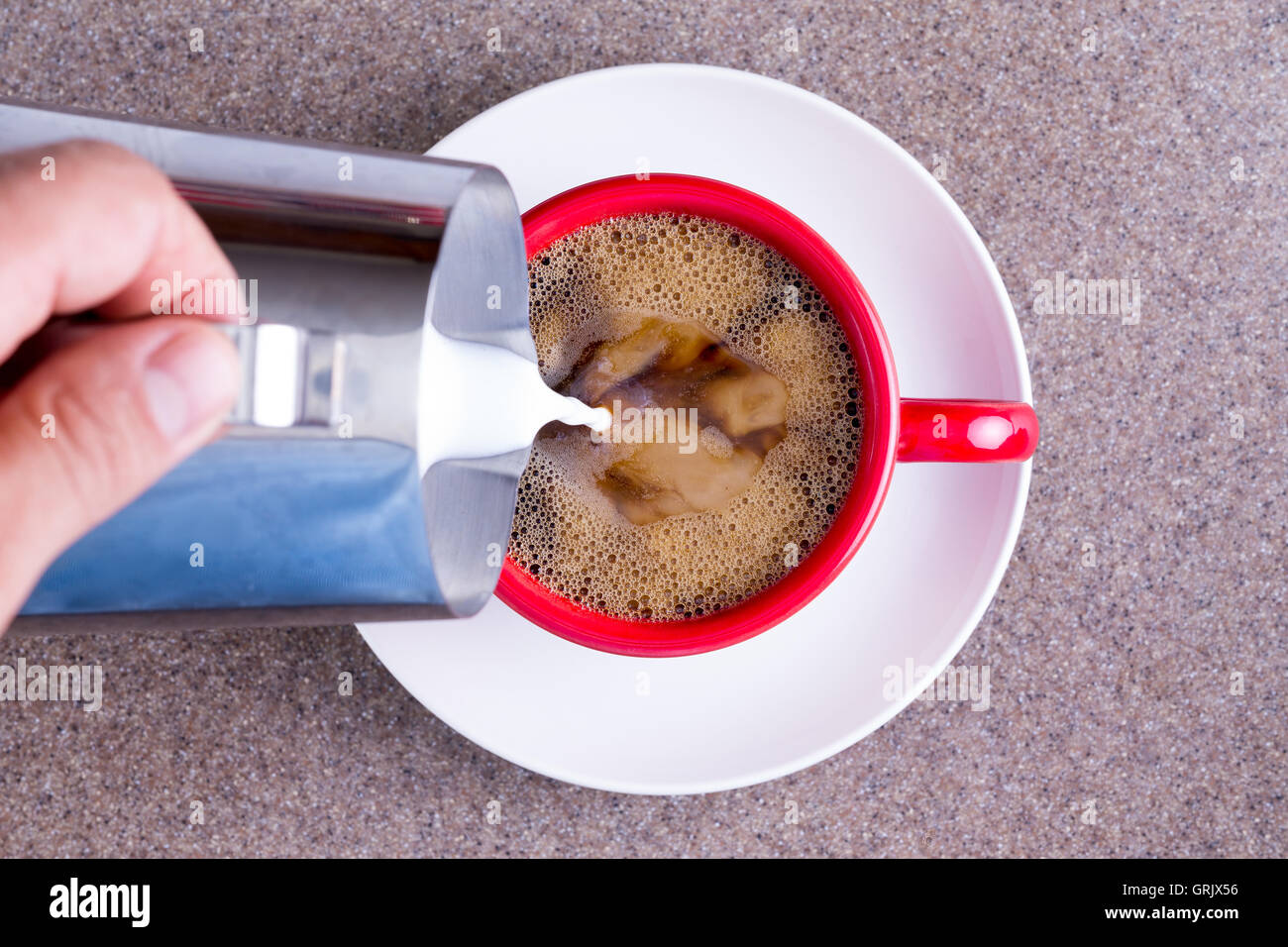 Verser le lait d'un homme dans une tasse de noir fraîchement moulu ou filtre à café expresso dans une tasse rouge sur une soucoupe blanche contre Banque D'Images