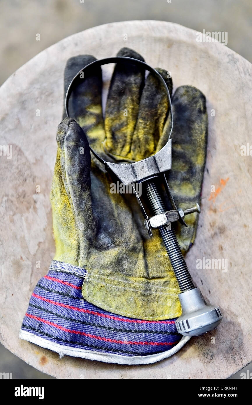 Le gant du travailleur sale tenant une clé de filtre à huile sur une planche en bois dans un atelier Banque D'Images