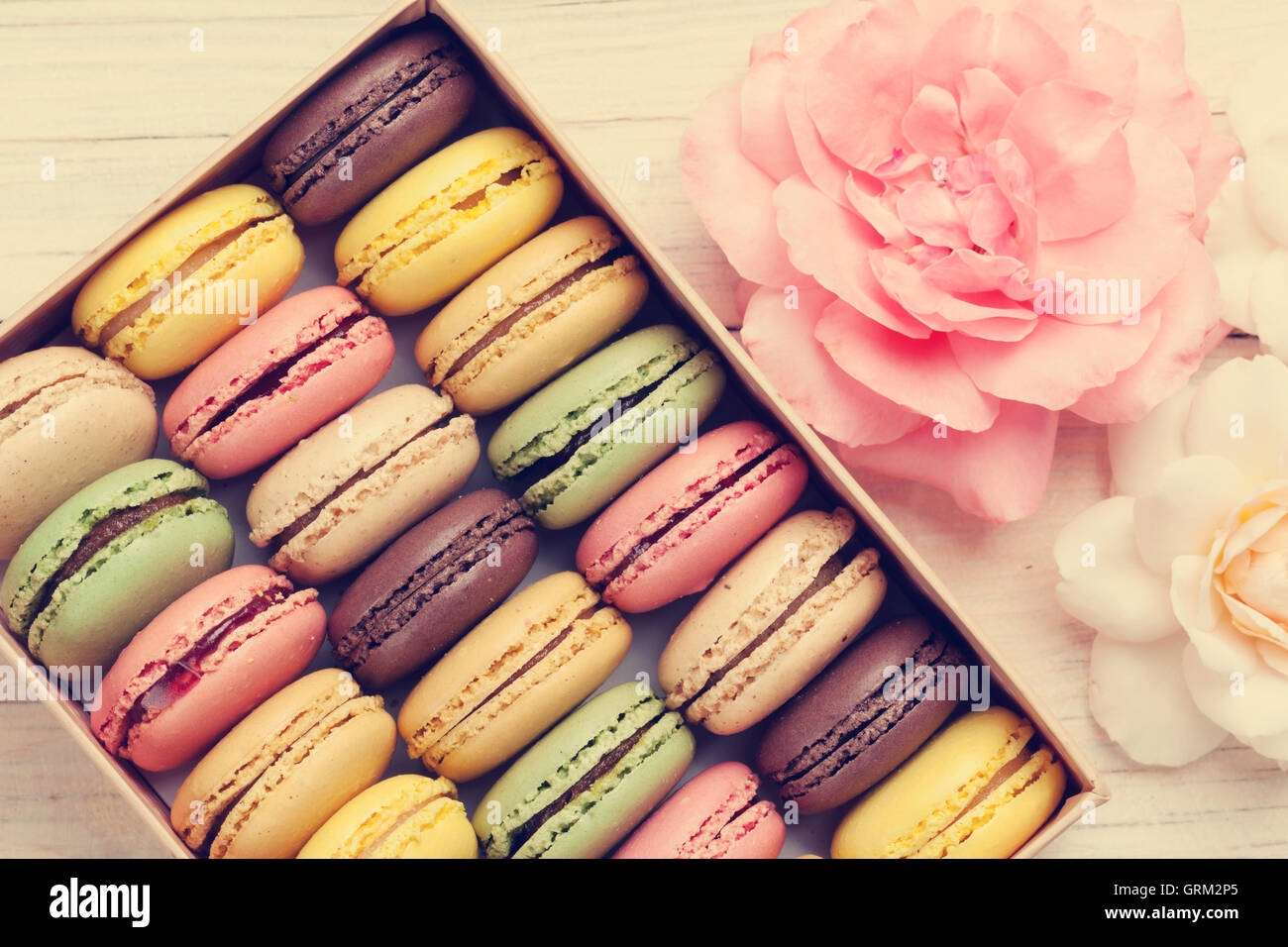 Macarons colorés et rose fleurs sur table en bois. Macarons sucrés en boîte cadeau. Vue d'en haut. Tons rétro Banque D'Images