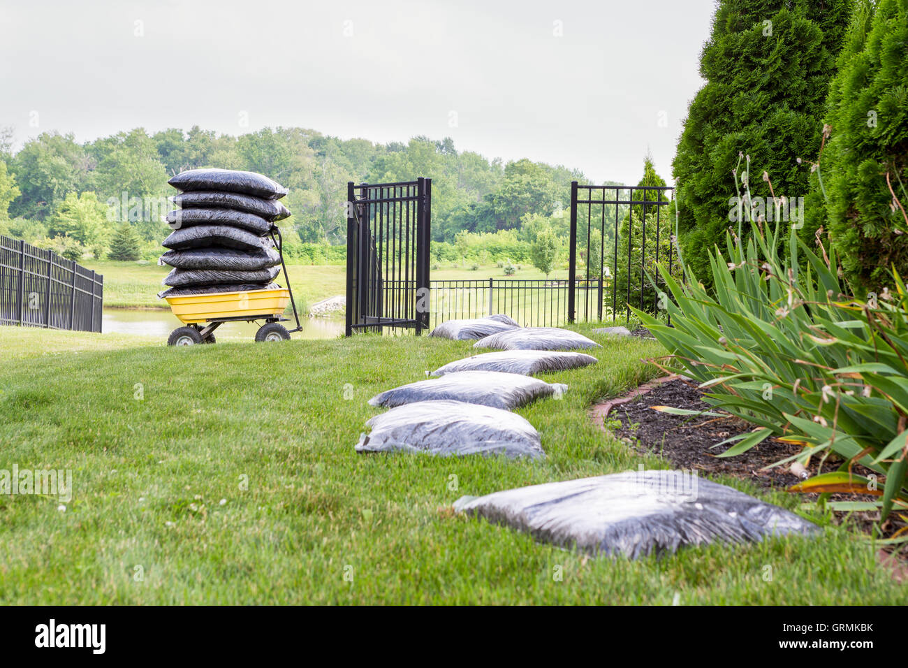 Le paillage du jardin prend du temps et des efforts avec des sacs de paillis disposés sur la pelouse à côté du parterre dans une longue rangée en attente Banque D'Images