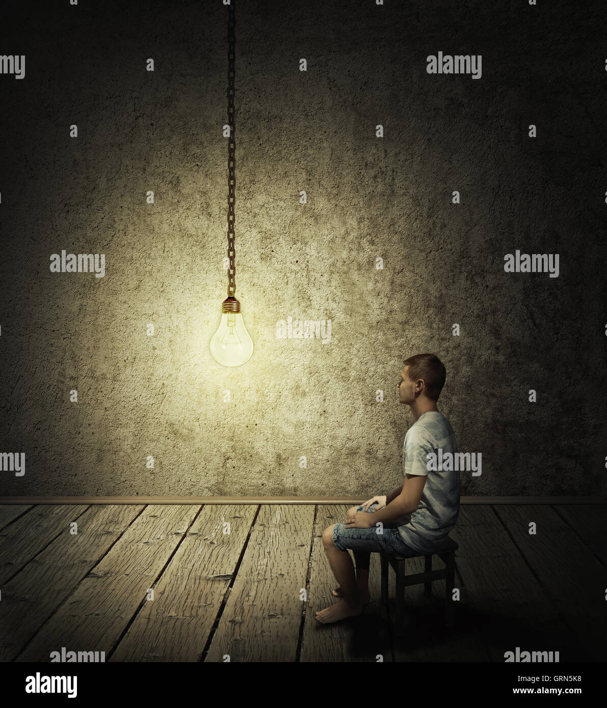 Idée créative concept avec un homme assis dans une pièce sombre, regardant une ampoule Banque D'Images