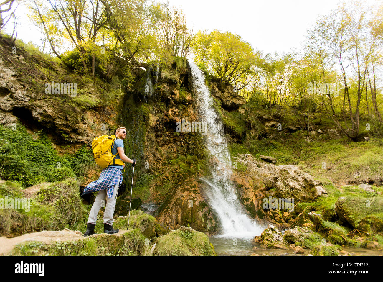 Jeune randonneur est arrêté près d'une cascade de montagne pour se reposer Banque D'Images