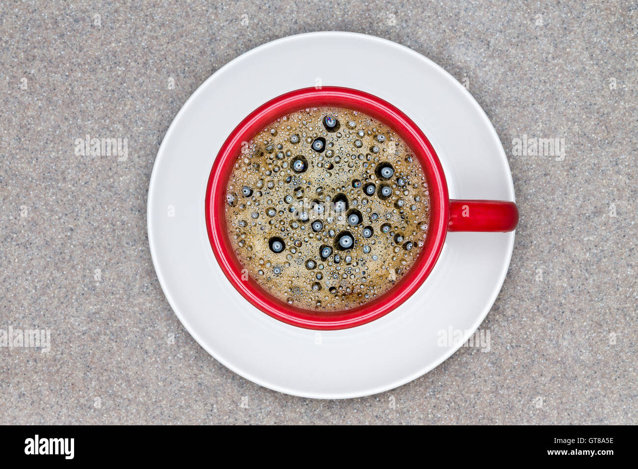 Vue aérienne de café noir chaud avec des bulles dans la tasse rouge sur le dessus de la plaque blanc servi sur table gris texturé. Banque D'Images