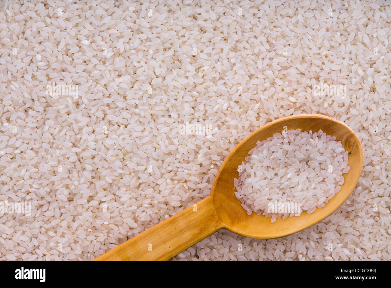 Grains de riz étuvé avec une cuillère de cuisine en bois rustique dans un contexte la texture des aliments Banque D'Images
