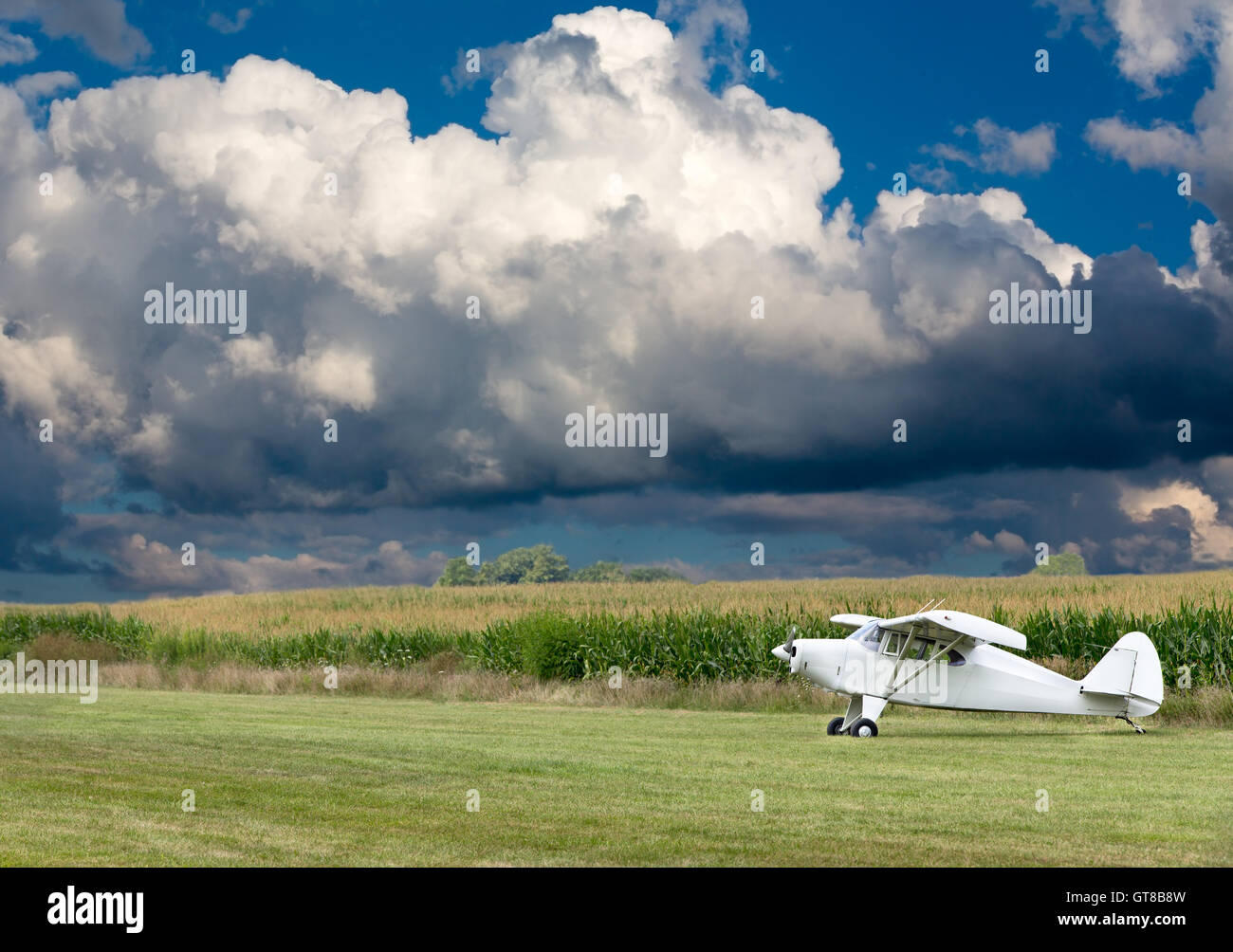 Petit avion ulm blanc prêt à décoller sur une zone rurale avec des champs de maïs à côté sous un nuage Cumulus spectaculaire forma Banque D'Images