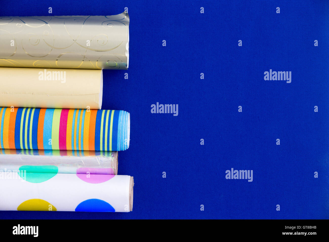 Rouleaux à motifs colorés et de papier d'emballage métallique disposés comme une frontière latérale sur un fond bleu avec copyspace Banque D'Images