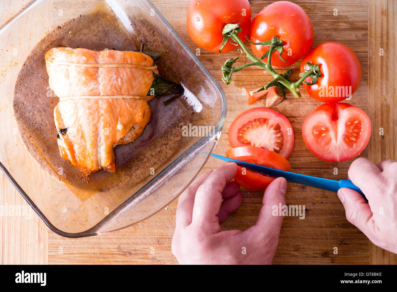 Chef de préparer un dîner gastronomique de tranchage saumon tomates fraîches pour accompagner le succulent filet de poisson dans le plat à four en verre Banque D'Images