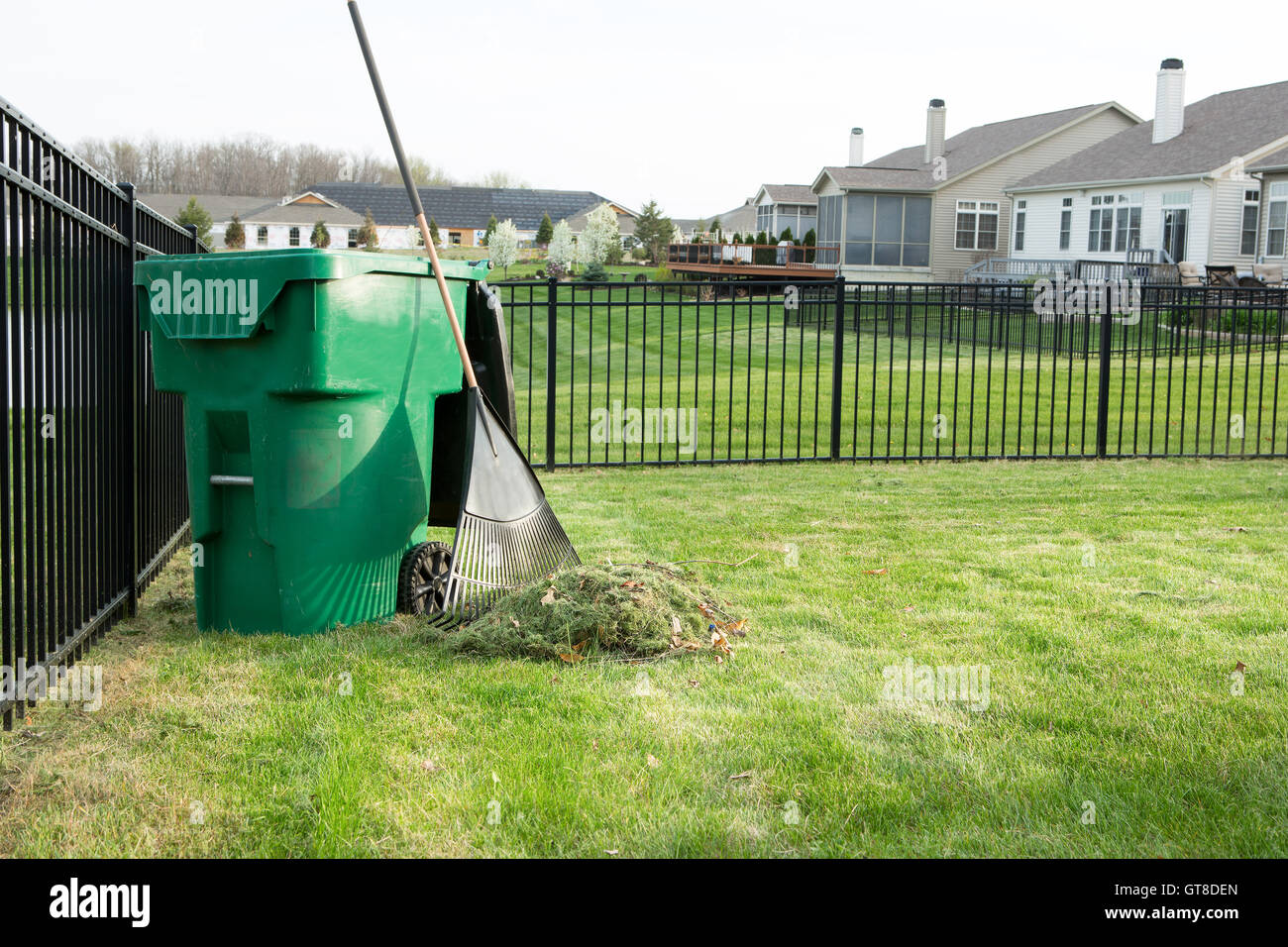 Ratissage des coupures de gazon sur un beau quartier résidentiel de banlieue avec un tas d'herbe à côté d'une coupe appuyée sur un râteau gree Banque D'Images