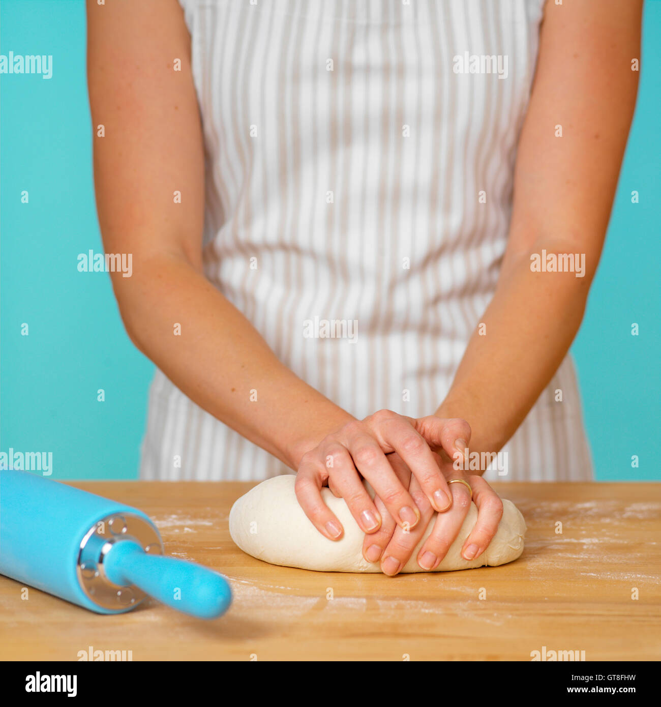 Femme en Tablier à rayures sur la surface en bois de pâte à pétrir avec Blue Rolling Pin Banque D'Images