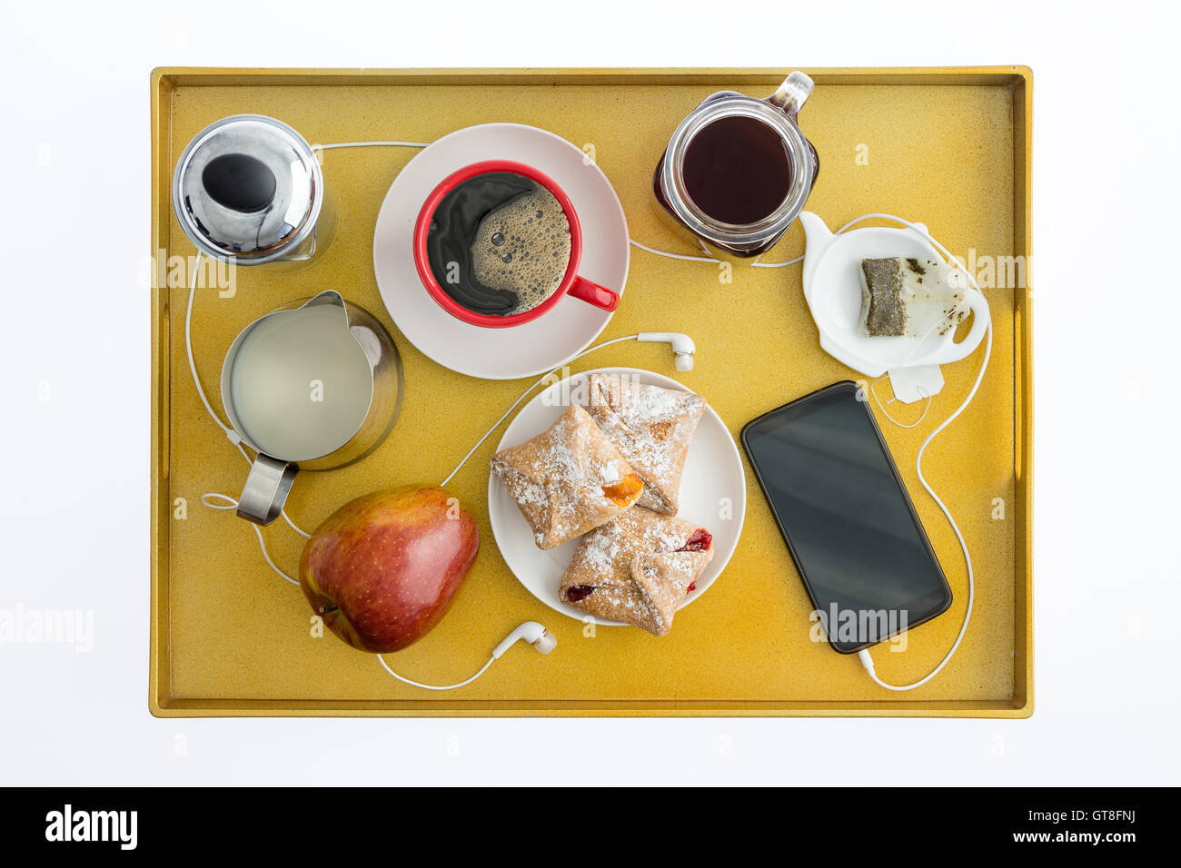 High Angle View of Smart Téléphone portable avec écouteurs distribués sur plateau de petit-déjeuner avec thé, café, pâtisseries et une pomme Banque D'Images