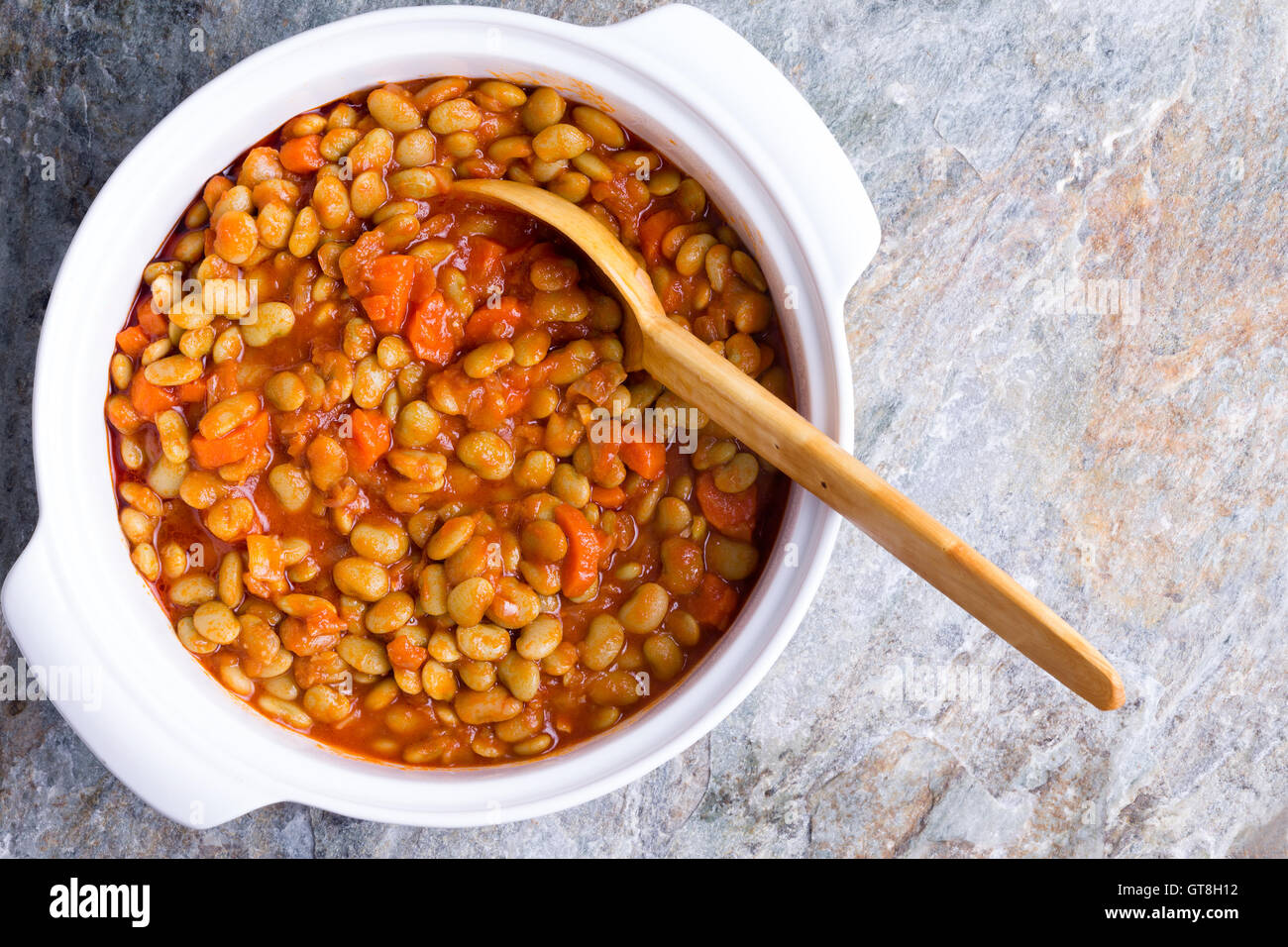 Casserole de haricots de lima bébé avec carottes servi dans un plat en céramique blanche avec une cuillère en bois servant sur un comptoir en pierre texturés, vo Banque D'Images