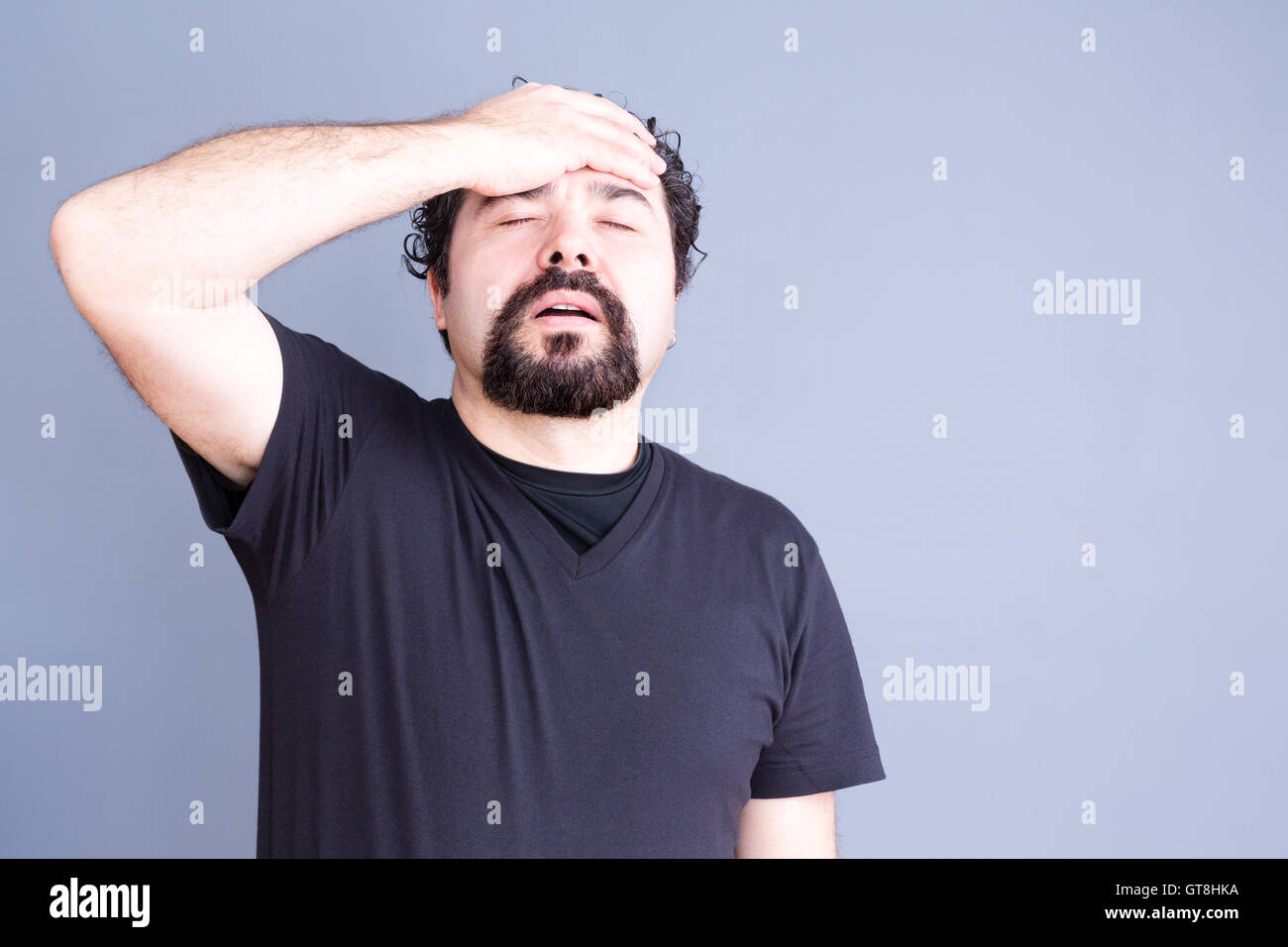 Jusqu'à la taille de l'homme regret frustré avec Barbe portant des T-Shirt tenue tête et part sur le front en studio avec Gray Backg Banque D'Images
