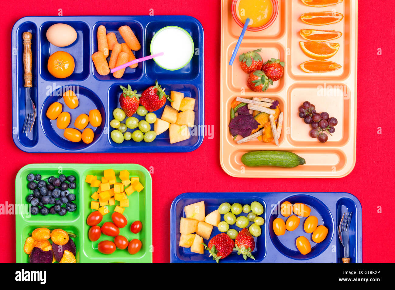 Quatre bleu, vert et rose le déjeuner en plastique rempli de plateaux de fruits et des légumes colorés le long du côté le lait et les jus Banque D'Images