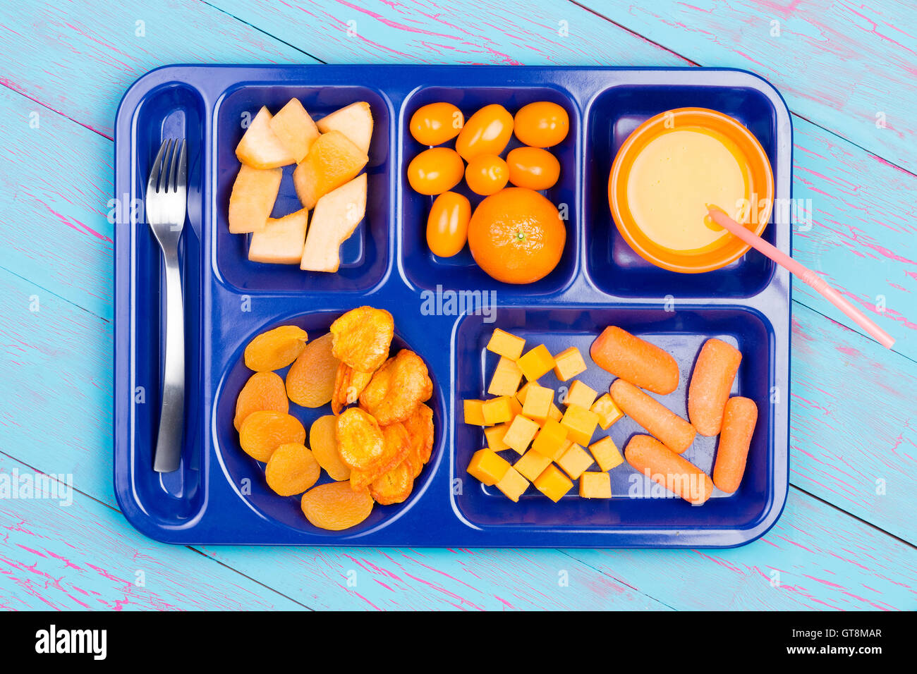 Un assortiment de fruits frais et secs coupés en petits morceaux et le jus d'orange en couleurs sur le plateau en plastique bleu avec fourche en acier inoxydable o Banque D'Images
