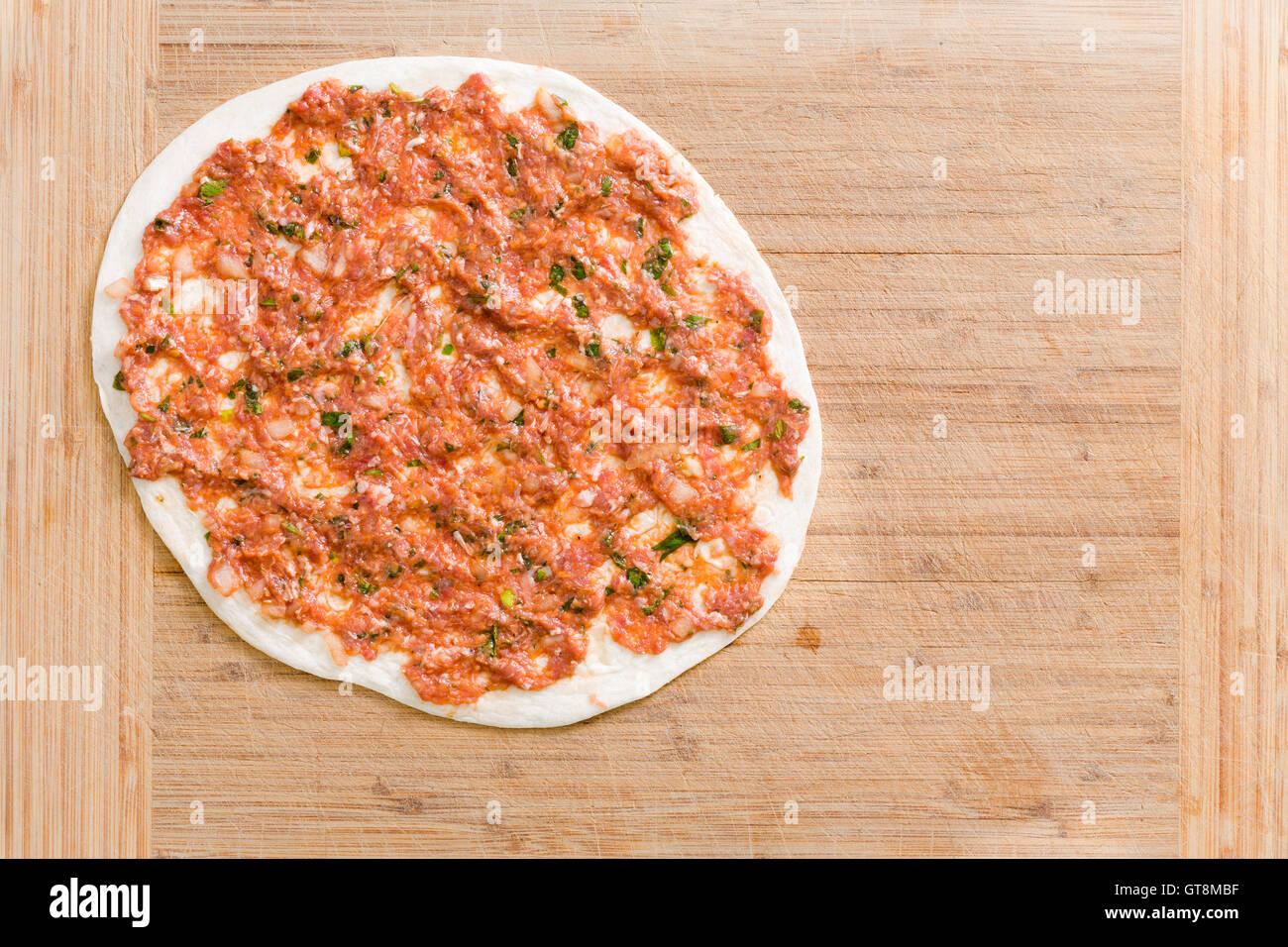 Lahmacun traditionnel turc unique avec la viande hachée et de légumes sur une base de pâte prête à cuire sur une planche à découper en bois bo Banque D'Images