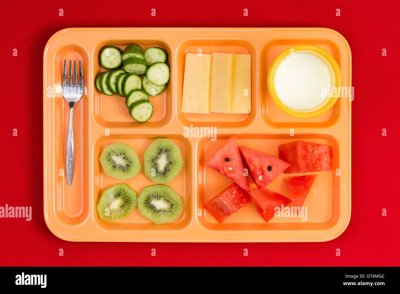 Vue perspective du haut vers le bas sur la taille de l'enfant en plastique lumineux déjeuner plateau avec fourche, concombre, fromage, kiwi, pastèque et tranches littl Banque D'Images