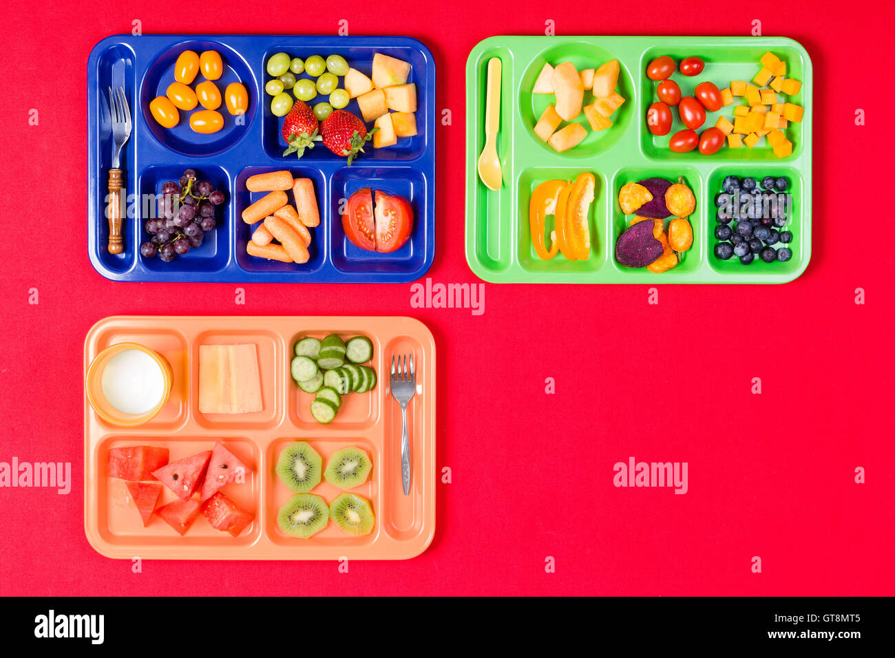 Trois enfants colorés en plastique rempli de plateaux repas tomates, raisins, melon d'eau et d'autres produits sur fond rouge avec l'exemplaire Banque D'Images