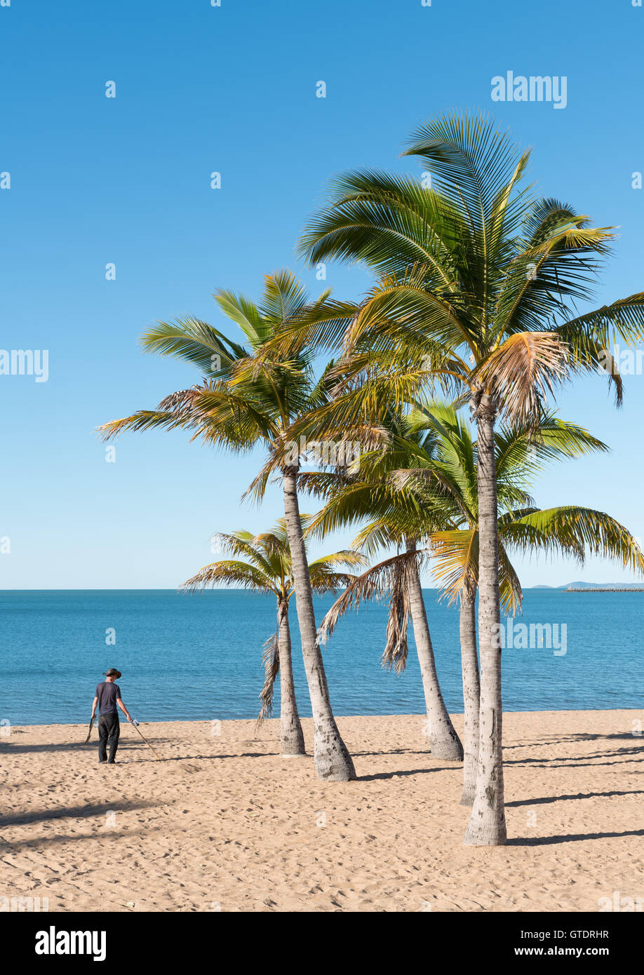 L'homme à l'aide de détecteur de métal sur belle plage tropicale sur le Strand, Townsville, Australie avec ciel bleu et la mer Banque D'Images