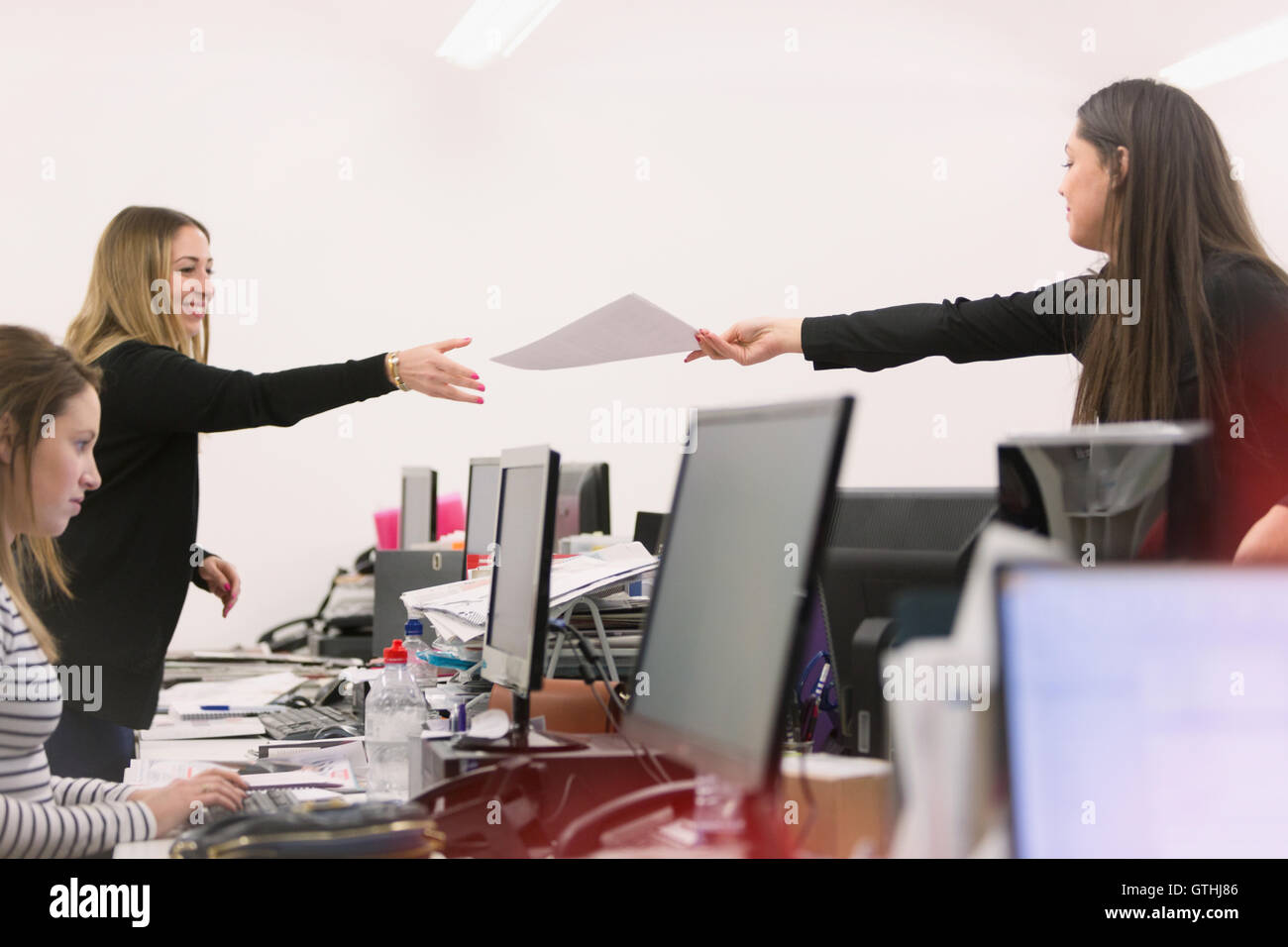 Businesswoman handing paperwork à collègue sur ordinateurs de bureau Banque D'Images