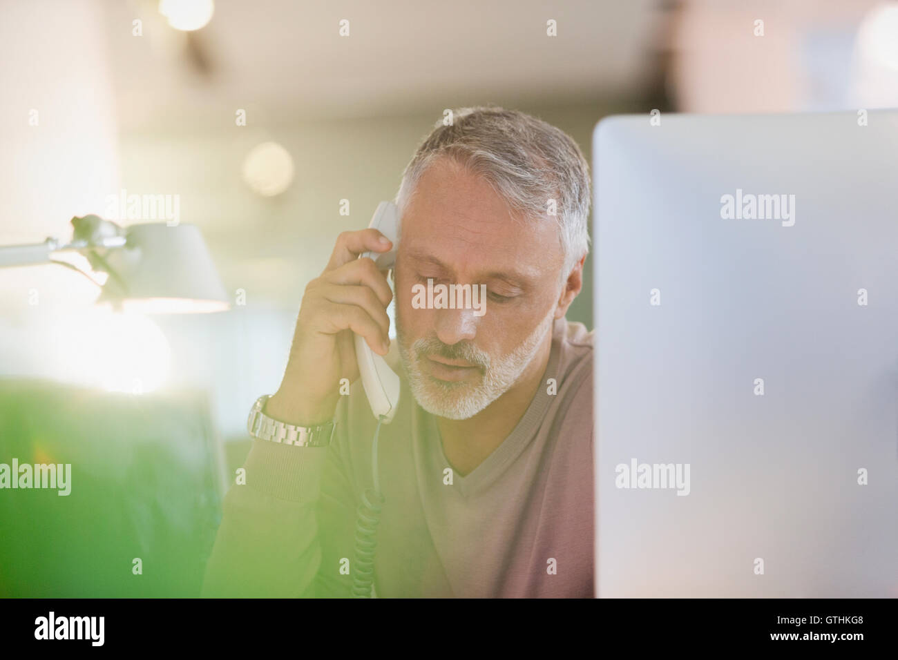 Businessman talking on telephone at computer in office Banque D'Images