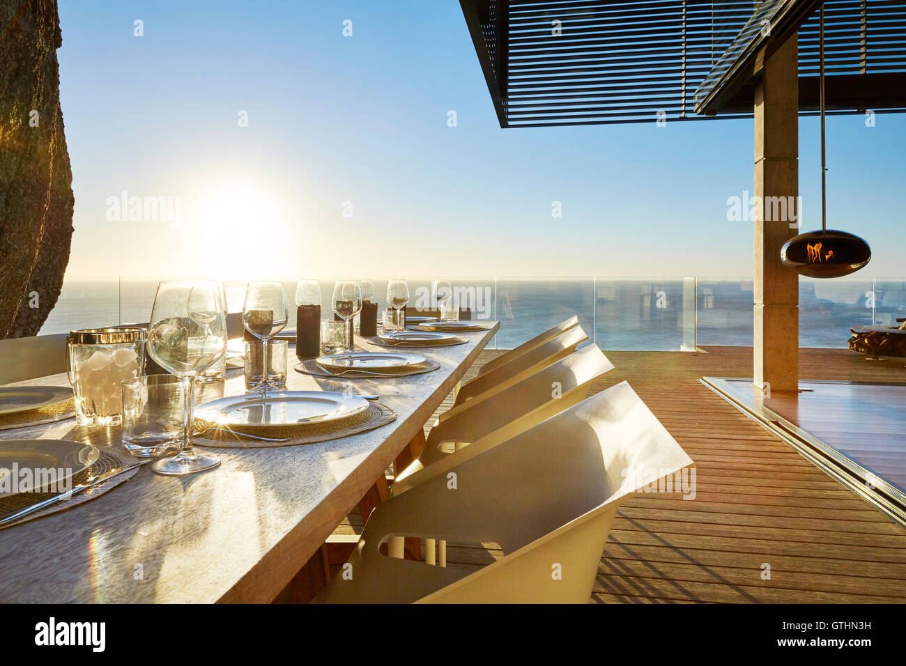 Soleil sur l'océan derrière luxury patio table à manger avec placesettings Banque D'Images