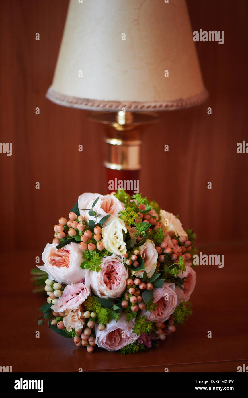 Bouquet de mariage forme classique, avec de la crème et de pivoine rose, baies roses renoncules sur la table de nuit à côté de la lampe Banque D'Images
