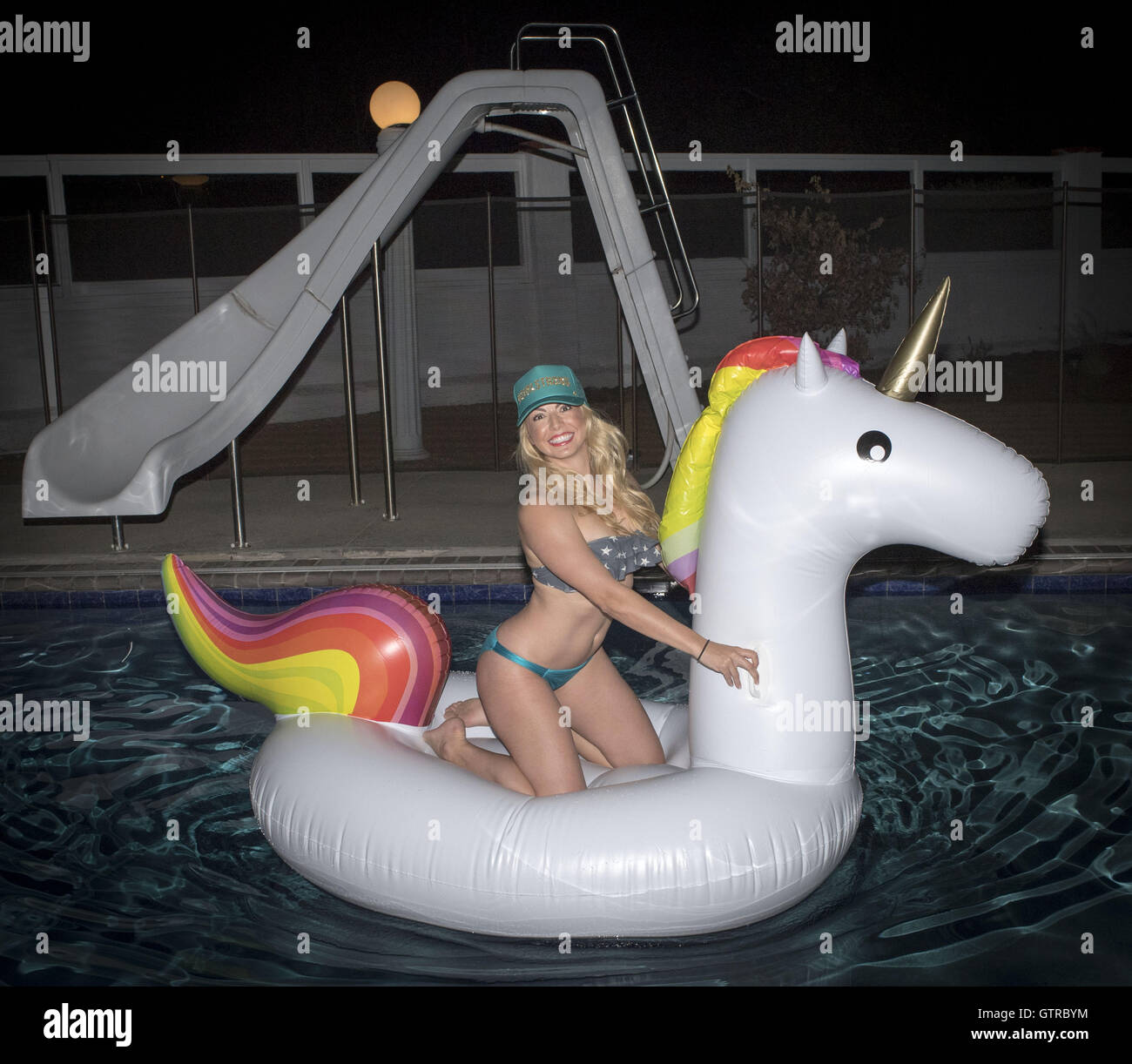 Orange County, Californie, USA. 3e, 2016 Sep. Une jolie jeune femme blonde portant un bikini et trucker cap se trouve sur un inflaitable licorne flottant dans une piscine la nuit. © David Bro/ZUMA/Alamy Fil Live News Banque D'Images