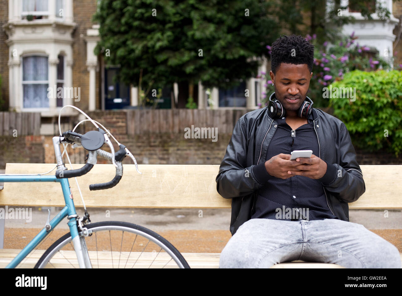 Jeune homme de lire ses messages texte s'assit sur un banc Banque D'Images