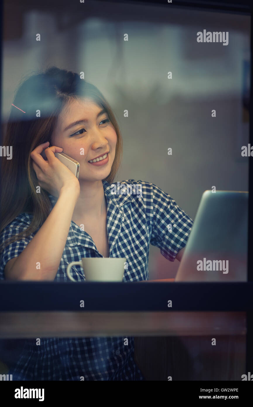 Portrait de l'Asie joli sourire femme parlant au téléphone tout en restant assis dans un café et profiter du café, du concept des vacances. Banque D'Images