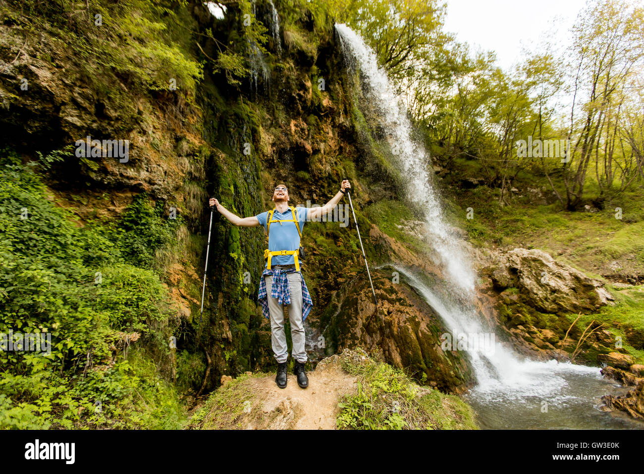 Jeune randonneur est arrêté près d'une cascade de montagne pour se reposer Banque D'Images