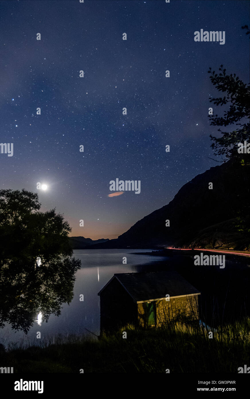 Avis de Llyn Lac Ogwen la nuit avant le lever du soleil avec ciel bleu, la lune et les étoiles. Maison dans le lac et des arbres. Banque D'Images