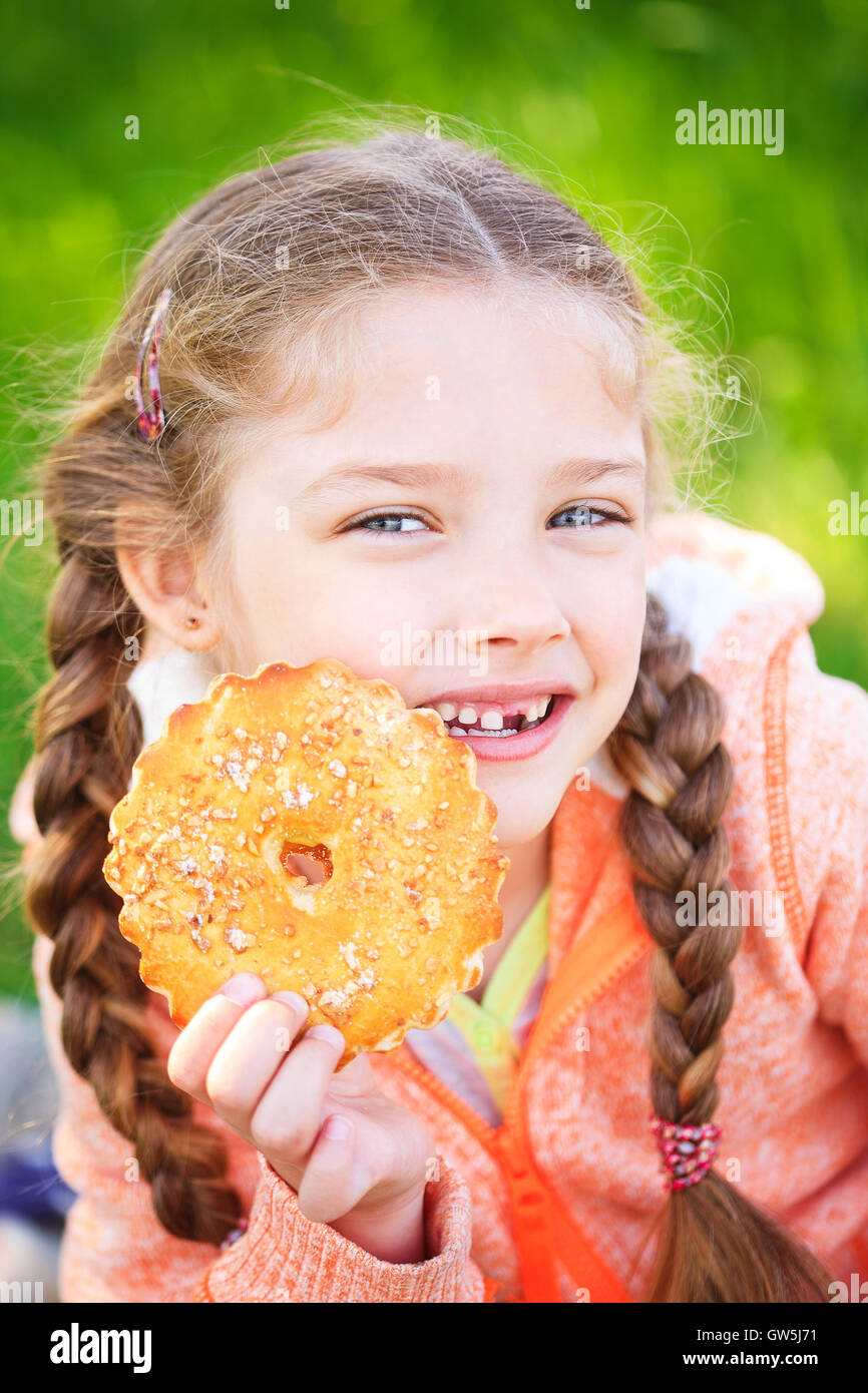 Douce jeune fille avec une dent tombée holding cookies dans sa main sur la nature Banque D'Images