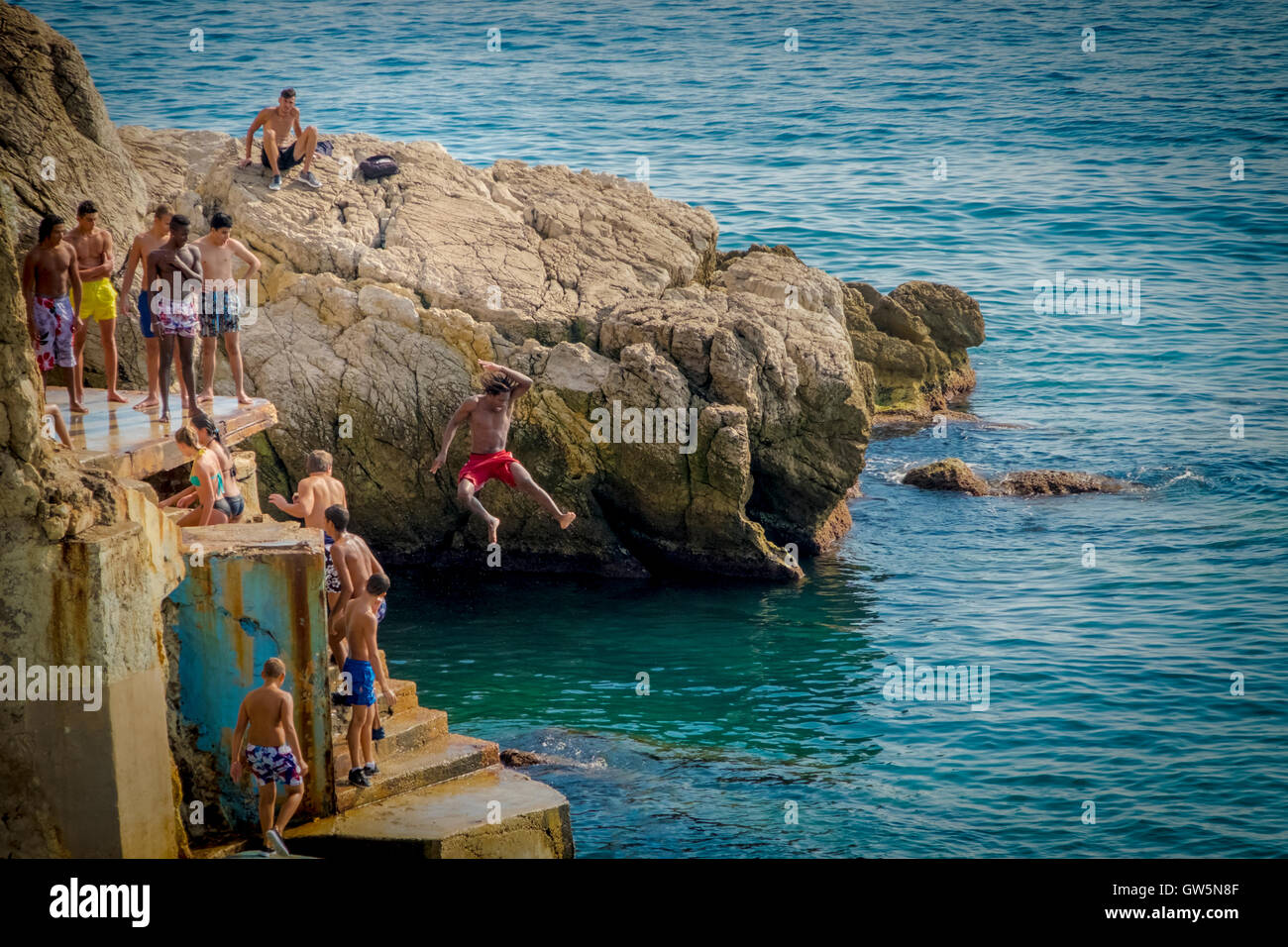 Les jeunes garçons dive off une plate-forme dans les eaux bleues de la mer Méditerranée tandis que d'autres regardent et attendent leur tour Banque D'Images