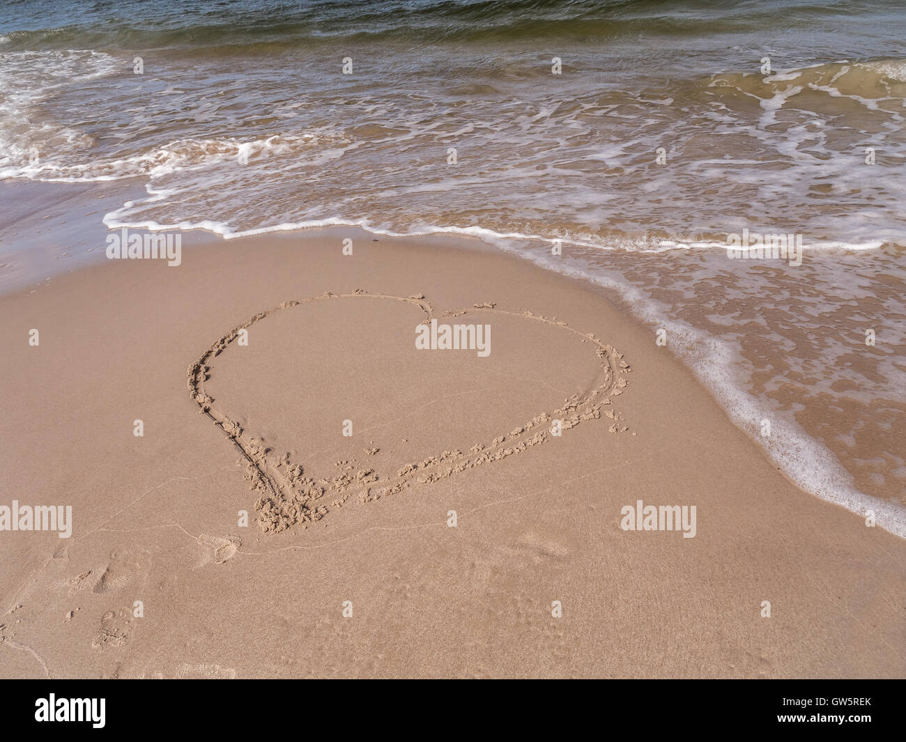 Coeur dessiné à la main sur la plage de sable avec la prochaine vague Banque D'Images