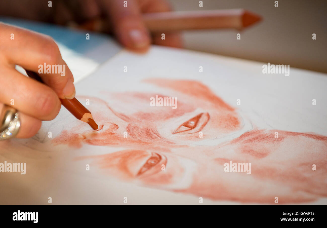 La main de la jeune femme de faire un portrait au crayon, à l'aide de la craie rouge sanguine (technique). Banque D'Images