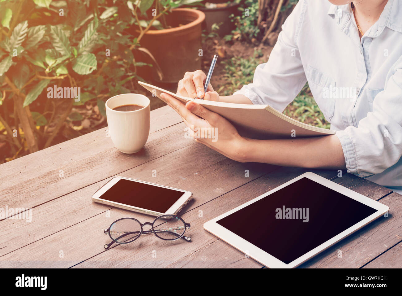 Main femme écrit ordinateur portable et téléphone, tablette sur la table dans le jardin du coffee shop avec tons vintage. Banque D'Images