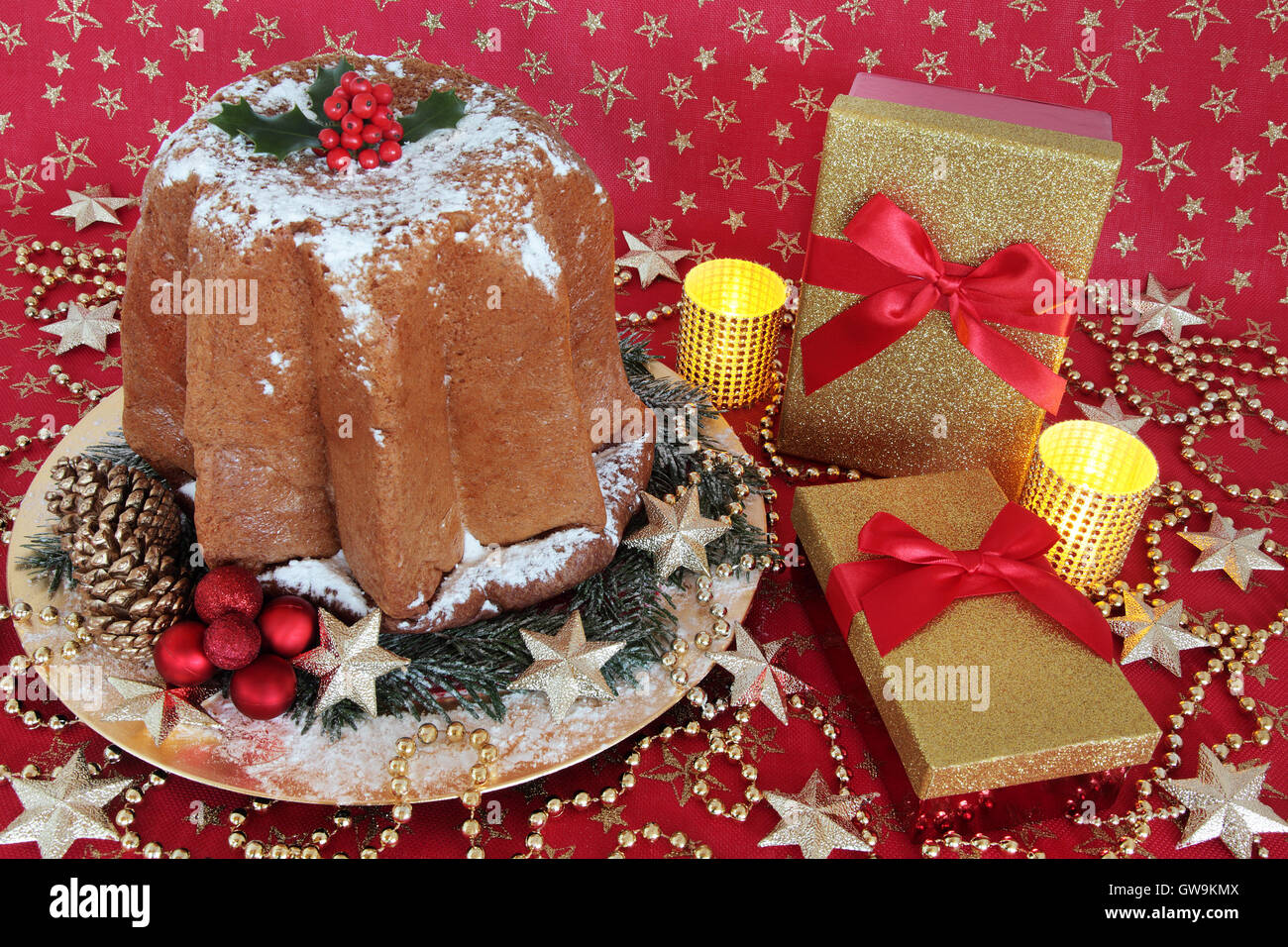 Gâteau de noël pandoro italien avec Holly, coffrets cadeaux, décorations babiole rouge et or et des bougies. Banque D'Images