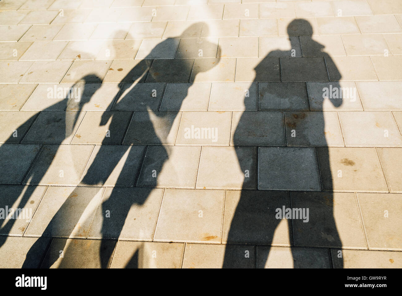 Les gens casting shadows sur le trottoir, quatre jeunes hommes et femmes d'éclipser des tuiles béton de la rue Banque D'Images