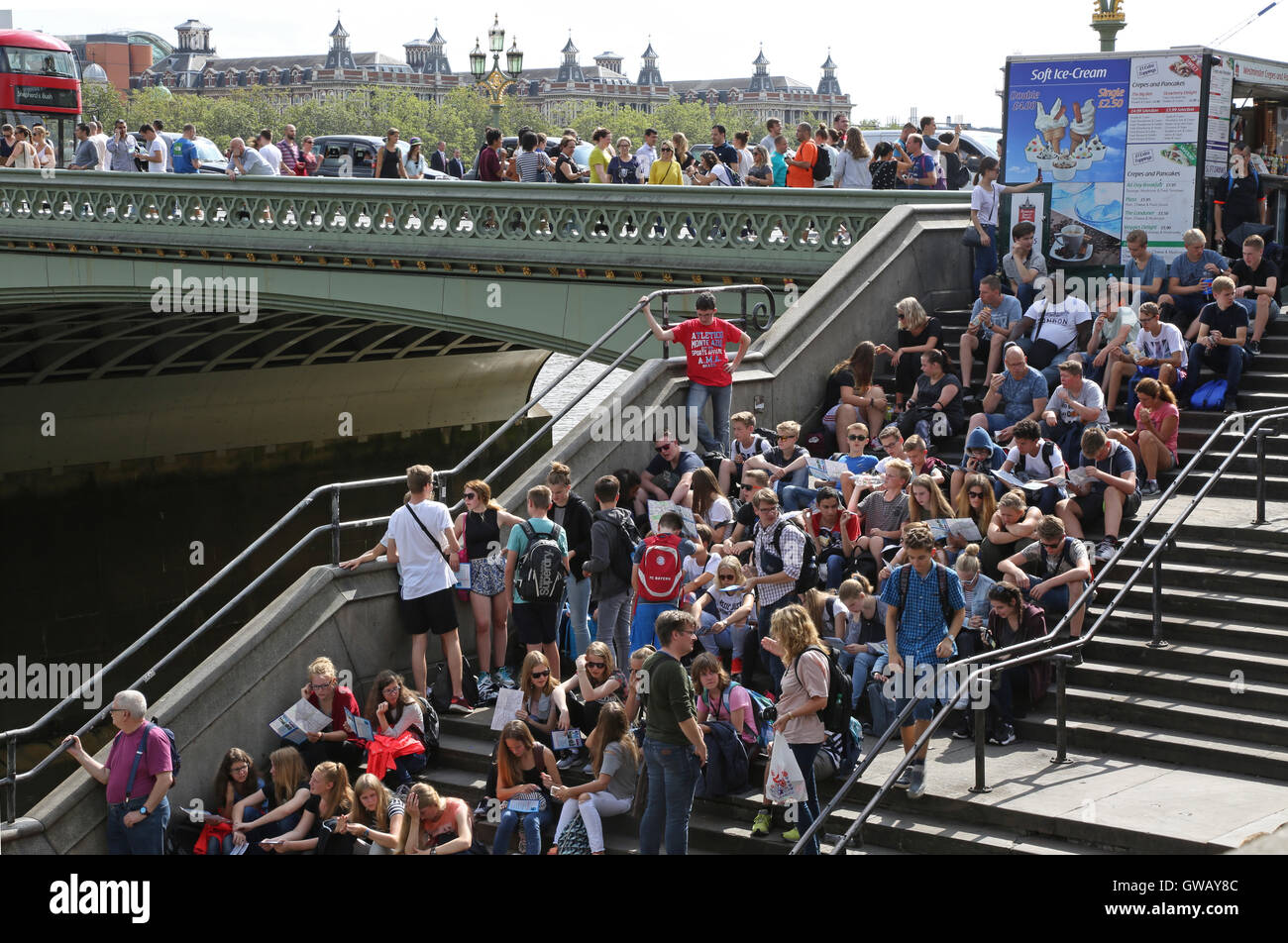 Des foules de jeunes touristes et visiteurs de s'asseoir sur les marches de Westminster Bridge, Londres, à côté de Big Ben et la Tamise Banque D'Images