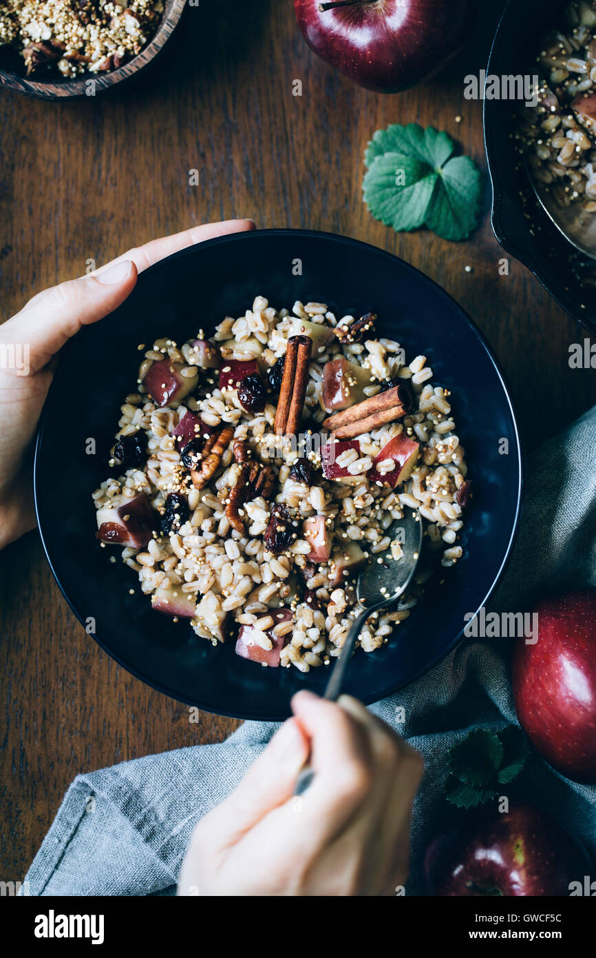 A womans mains sont photographiés comme elle est sur le point de manger un bol de petit-déjeuner chaud Farro bol avec des pommes à la cannelle. Banque D'Images