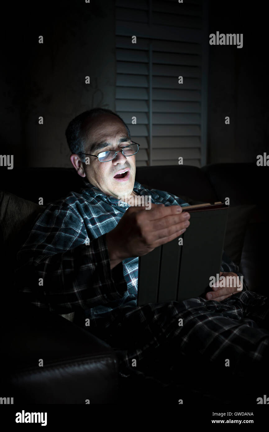 Le bâillement middle aged man wearing pajamas Tablette de lecture la nuit au lit Banque D'Images