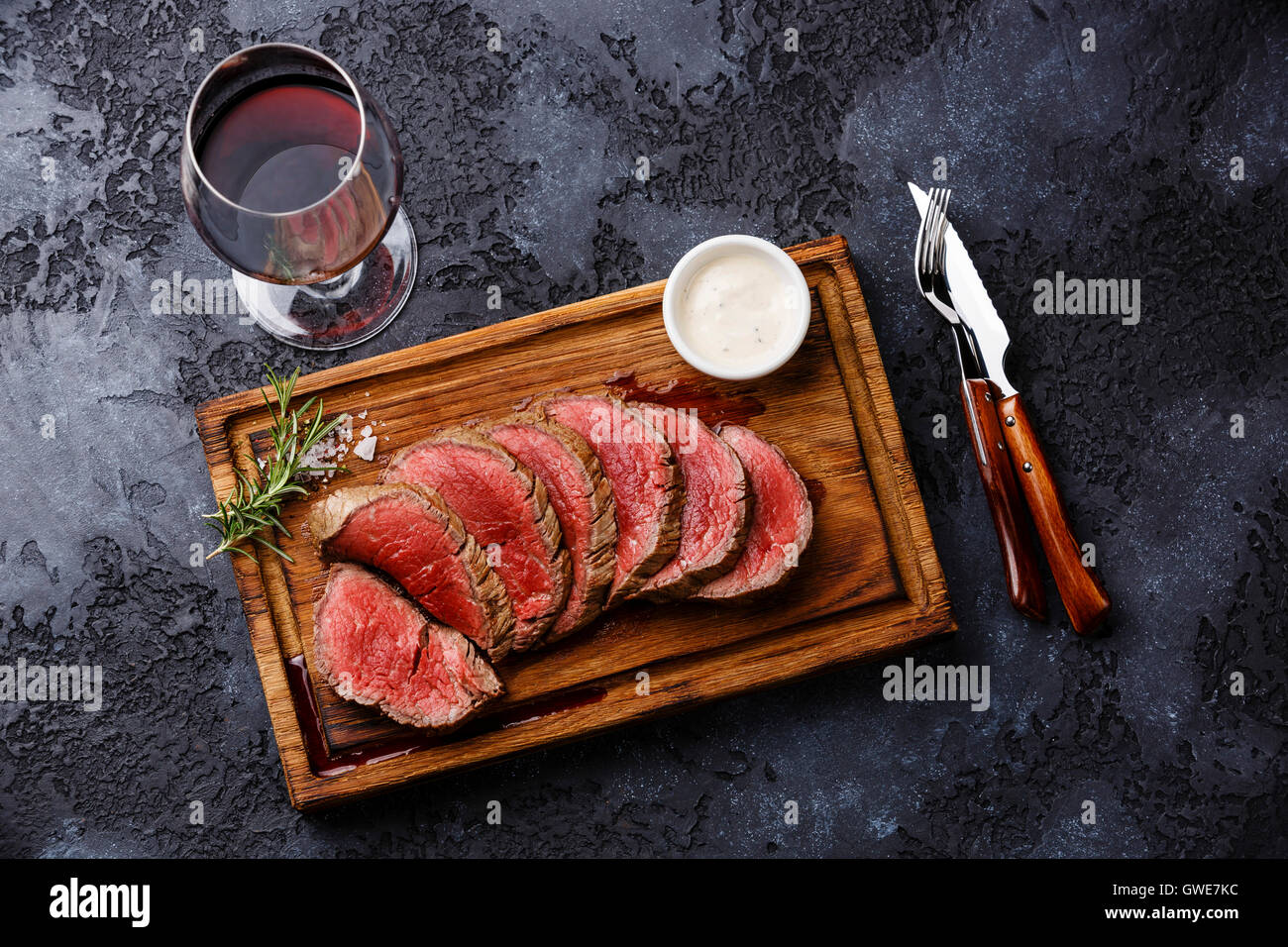 Tranches de filet mignon grillé Steak roastbeef et sauce au piment sur planche à découper en bois et le vin rouge sur fond sombre Banque D'Images