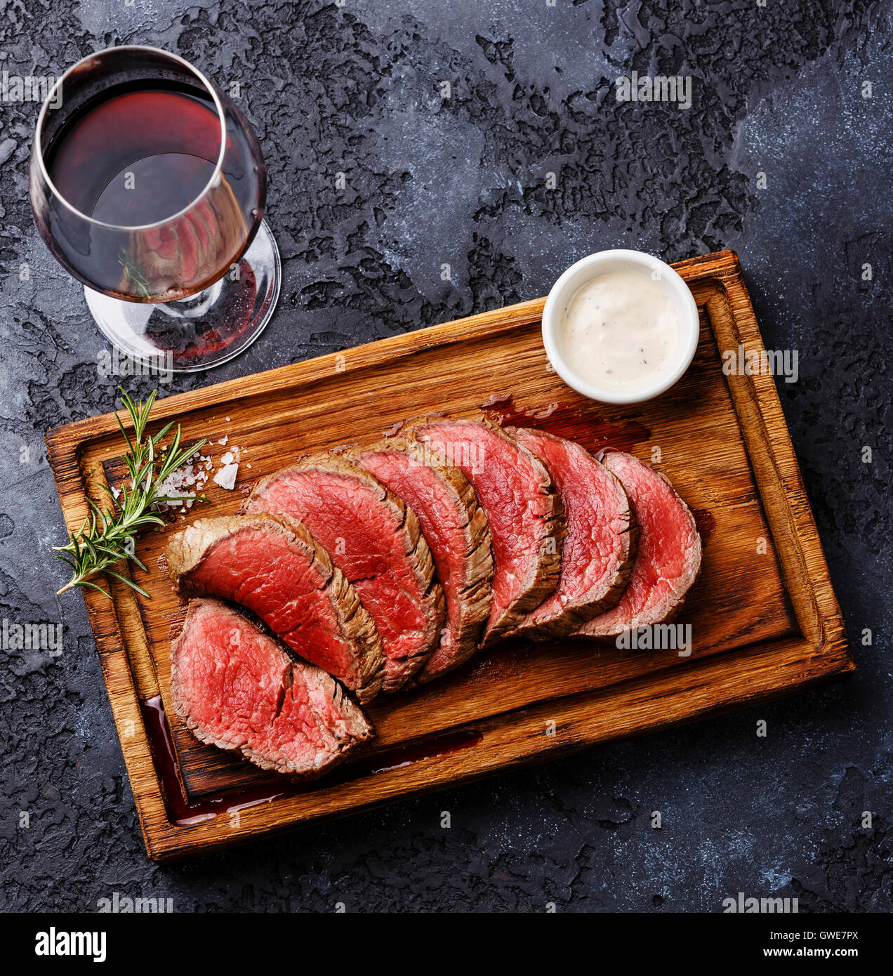 Tranches de filet mignon grillé Steak roastbeef et sauce au piment sur planche à découper en bois et le vin rouge sur fond sombre Banque D'Images