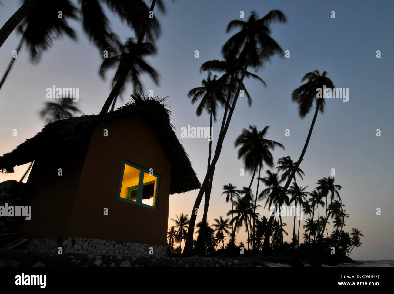 Une hutte solitaire avec des arbres en silhouette au coucher du soleil. Banque D'Images