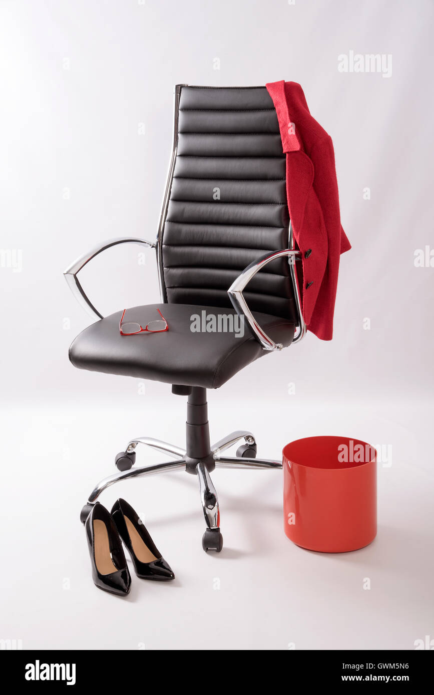 Un fauteuil en cuir noir avec un manteau rouge poubelle, hautes chaussures de talon et une paire de lunettes sur le siège Banque D'Images